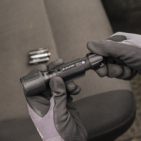 Person wearing gloves holding a black tool with a blurred background